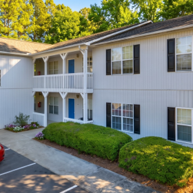 Exterior of apartment community in Butner, NC featuring two-story buildings with private entrances, on-site parking, landscaped grounds, and a peaceful wooded setting near local highways, shopping, and dining