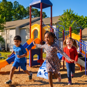 Children playing on playground at family-friendly apartment community with outdoor recreation space, located in a convenient neighborhood near schools, parks, and local amenities